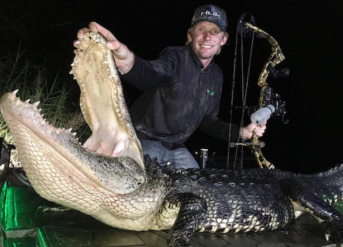 Man holding a large alligator he shot with a bow and arrow at night.