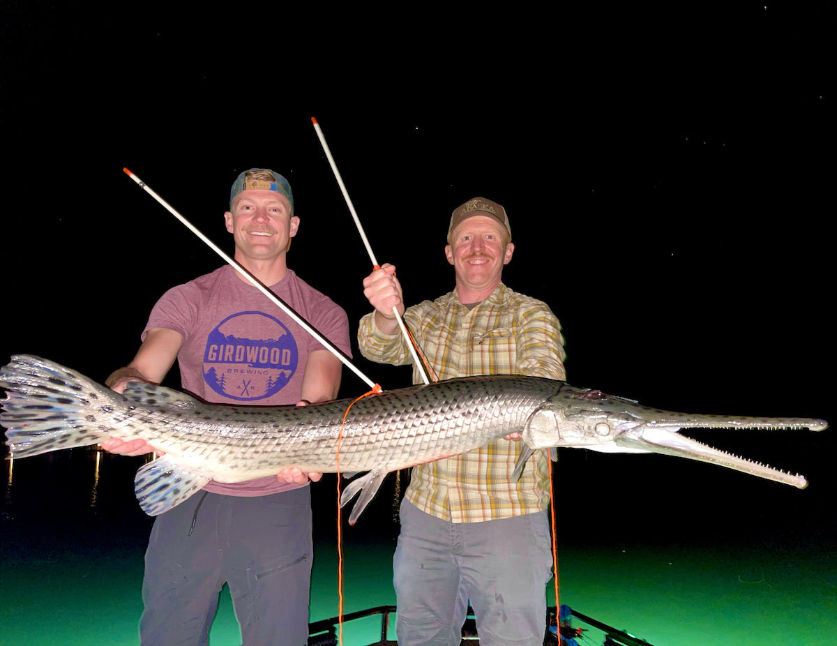 Two men posing with a giant longnose gar they shot together on a bowfishing charter.