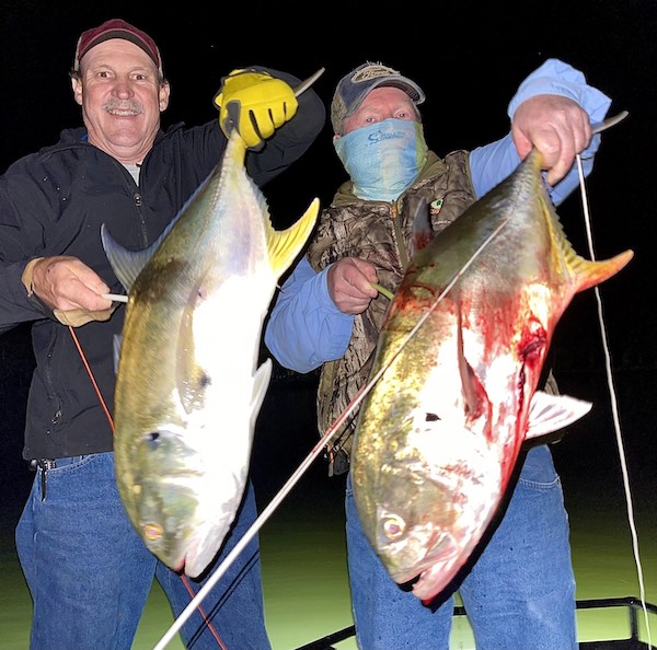 Two men holding jack crevalle they have shot with a bowfishing bow at night.