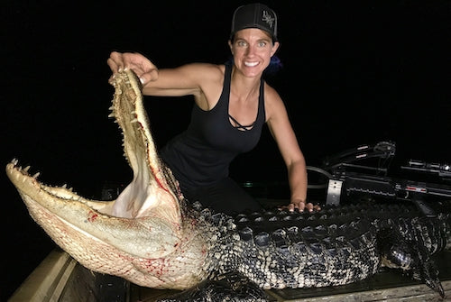 Woman posing with a trophy alligator she hunted at night on a bowfishing charter in Florida.