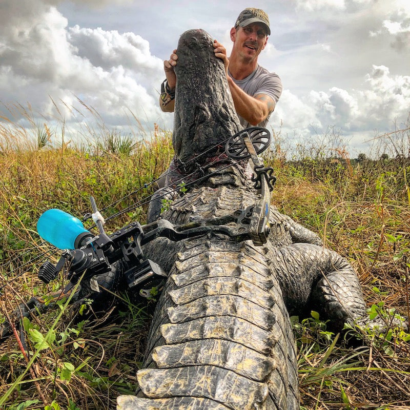 Man holding a large alligator he hunted with a bow and arrow in Florida. 