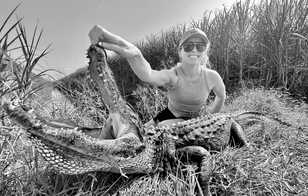 Woman holding a large alligator on a grassy bank in Florida. 
