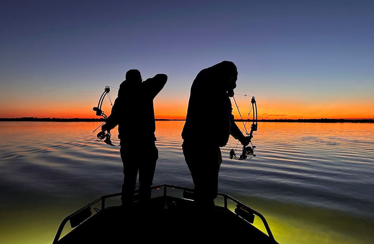Two people on a boat at sunset on a bowfishing charter. 