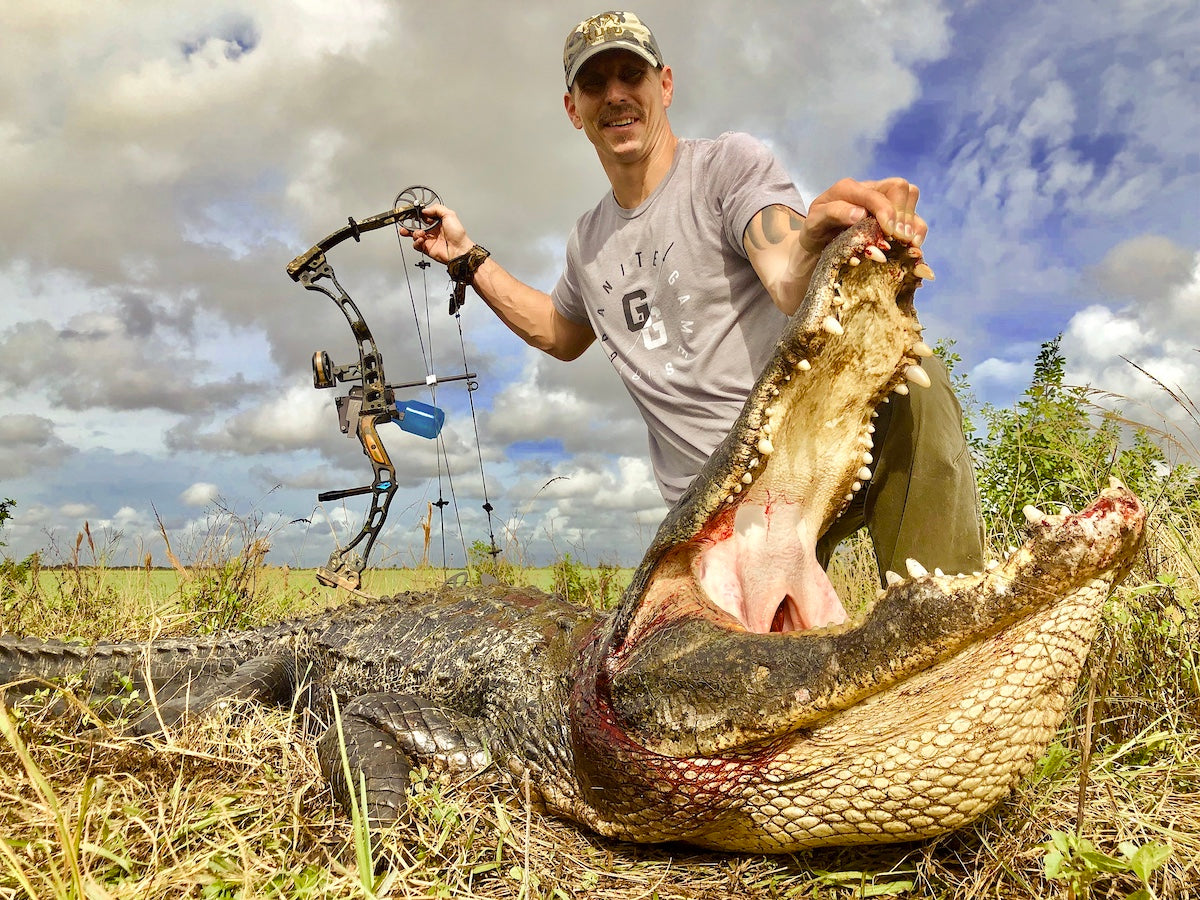 Man holding a large alligator with a bow and arrow after hunting in Florida.