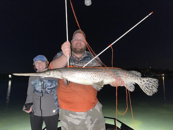 Two people holding a large longnose gar shot at night on a Florida Bowfishing Charter.